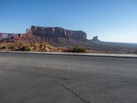 there is a lone motorcycle driving through the desert on a paved road near cliffs and buildings