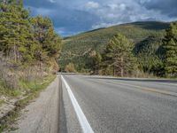 a person on a bike rides down the road with mountains in the distance along side of it