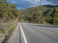 a person on a bike rides down the road with mountains in the distance along side of it