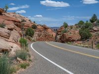 road with yellow markings running along the side of it near rocks in the desert landscape