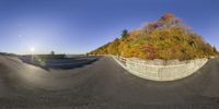 a fish eye view of a wide open road, with a wall surrounding it, and an autumn tree behind