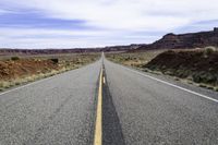 a narrow road stretches across two large mountains and the desert below it and is partly cloudy