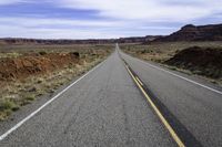 a narrow road stretches across two large mountains and the desert below it and is partly cloudy