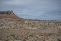 the view of a winding road through a desert area with tall rock formations in the distance