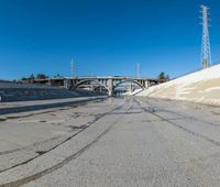 the empty street and dirt of a freeway under a blue sky with power lines overhead