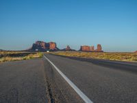 a truck driving down an empty country road in the desert under a bright blue sky