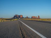 a truck driving down an empty country road in the desert under a bright blue sky