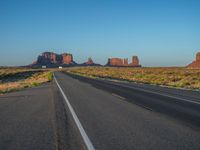 a truck driving down an empty country road in the desert under a bright blue sky