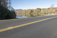 the empty road is next to the water and trees that are reflected in the lake