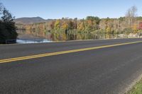 the empty road is next to the water and trees that are reflected in the lake