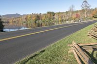 the empty road is next to the water and trees that are reflected in the lake