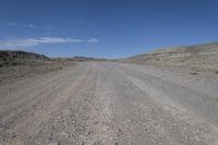 a dirt road is surrounded by some hills and desert like terrain as the vehicle sits on it