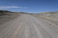 a dirt road is surrounded by some hills and desert like terrain as the vehicle sits on it