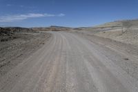 a dirt road is surrounded by some hills and desert like terrain as the vehicle sits on it