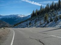 there is snow on the ground and the mountain side on the road, with some trees growing on it