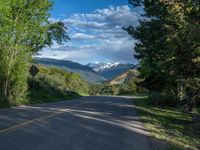 the road winds up on the mountainside on a sunny day with beautiful clouds and trees