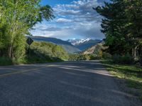 the road winds up on the mountainside on a sunny day with beautiful clouds and trees