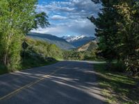 the road winds up on the mountainside on a sunny day with beautiful clouds and trees