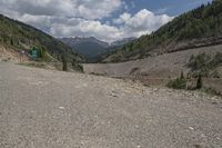 the road is empty with trees and mountains behind it, and the gravel has not been raked