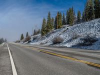 a lone motorcycle on the road during the day in mountains with trees and snow covering the road