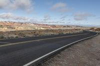 an empty open highway with mountains in the background and cloudy skies above its tops