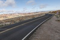 an empty open highway with mountains in the background and cloudy skies above its tops