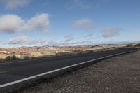 an empty open highway with mountains in the background and cloudy skies above its tops