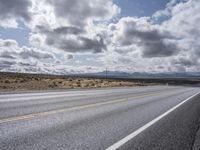 an empty highway with two yellow lines in the middle of it and mountains in the distance