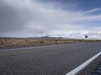 a long empty street in the desert, with a sign and other hills beyond the road