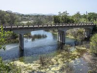 a view from a bridge overlooking trees and a mountain range of hills behind a bridge