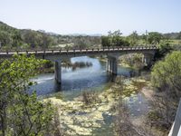 a view from a bridge overlooking trees and a mountain range of hills behind a bridge