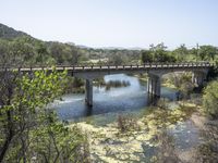 a view from a bridge overlooking trees and a mountain range of hills behind a bridge