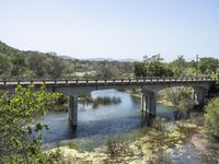 a view from a bridge overlooking trees and a mountain range of hills behind a bridge