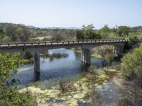 a view from a bridge overlooking trees and a mountain range of hills behind a bridge