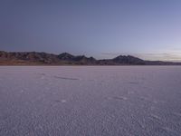 a large expanse of white sand in front of a desert with mountains in the background