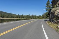 a road next to the lake in the mountains with trees on both sides of it