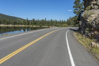 a road next to the lake in the mountains with trees on both sides of it