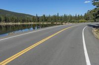 a road next to the lake in the mountains with trees on both sides of it