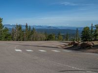 the mountains are visible in the distance from this wide, empty road, overlooking a wide landscape and forest