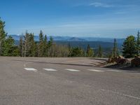 the mountains are visible in the distance from this wide, empty road, overlooking a wide landscape and forest