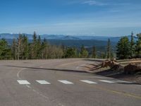 the mountains are visible in the distance from this wide, empty road, overlooking a wide landscape and forest