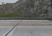 the highway is empty near the cliff face and green vegetation on it, surrounded by rocks and grass