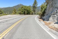 a man riding a scooter down a winding mountain road next to trees and a rock