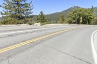 a man riding a scooter down a winding mountain road next to trees and a rock