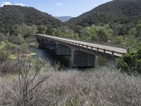 a view from a bridge overlooking trees and a mountain range of hills behind a bridge