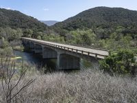 a view from a bridge overlooking trees and a mountain range of hills behind a bridge