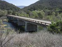 a view from a bridge overlooking trees and a mountain range of hills behind a bridge