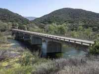 a view from a bridge overlooking trees and a mountain range of hills behind a bridge