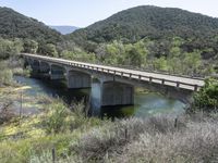 a view from a bridge overlooking trees and a mountain range of hills behind a bridge