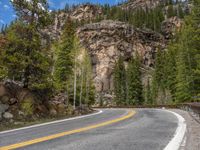 the curved road curves in front of a mountain area with pine trees behind it,